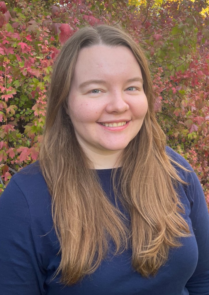 Headshot of white woman with long light brown hair, leaves in the background.